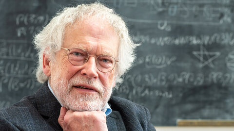 Portrait of Anton Zeilinger, looking thoughtful in front of a blackboard